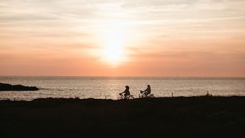Atardecer sobre el océano con dos personas en bicicletas silueteadas contra el cielo.