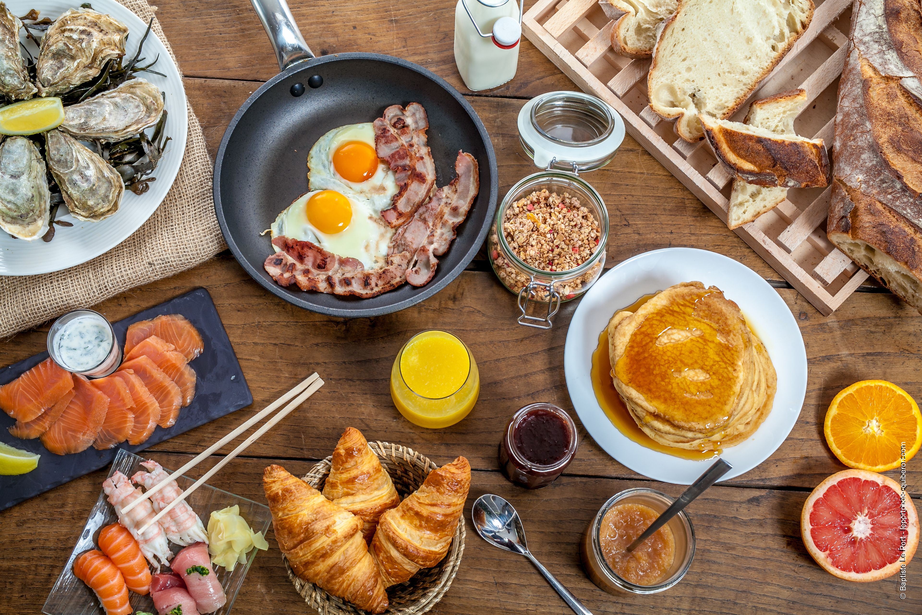A breakfast table with various foods including eggs, bacon, croissants, and orange juice.
