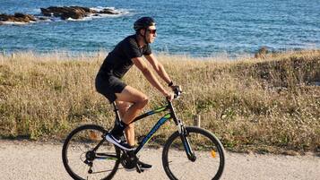 A person riding a bicycle on a coastal path with a view of the sea and rocks in the background.