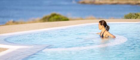 A woman in a swimming pool with a view of the sea and a distant shoreline.