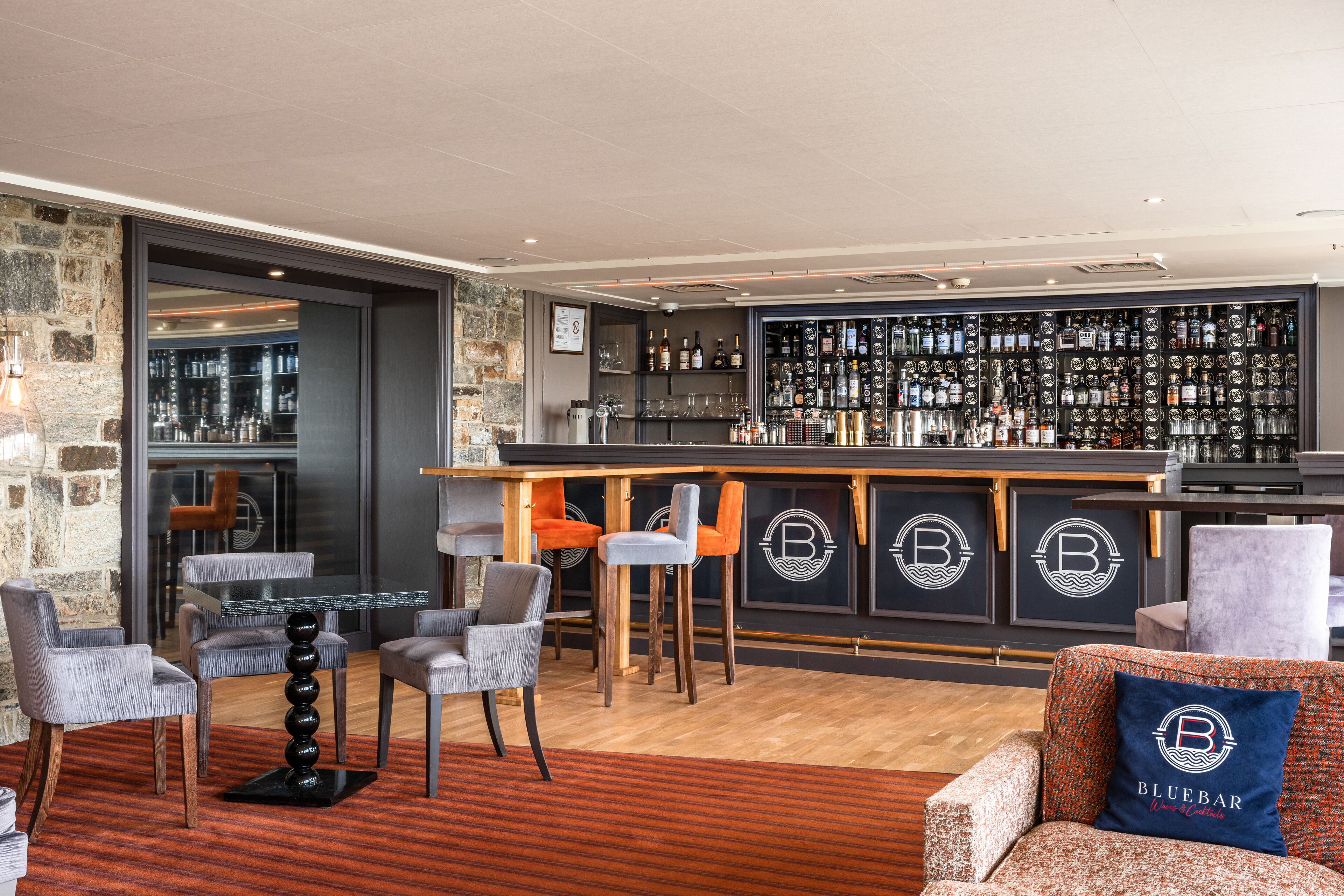 A bar area with a wooden bar counter, multiple bar stools, and a seating area with chairs and a sofa.