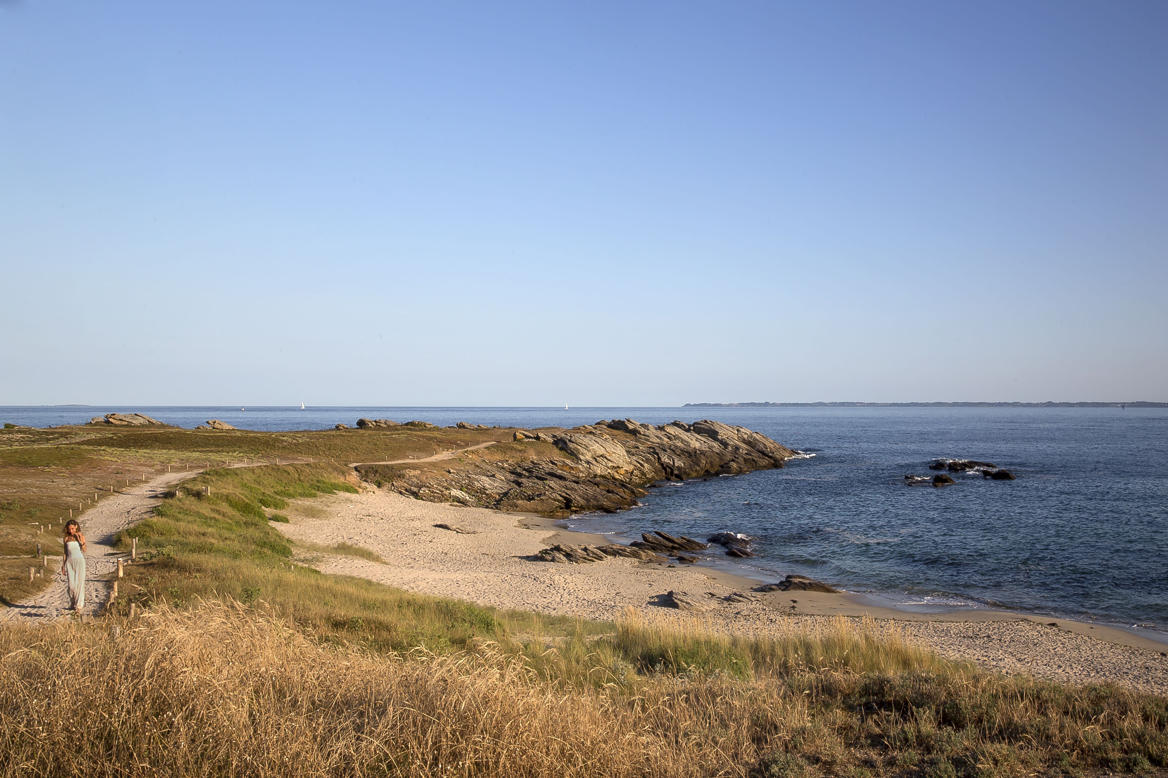 A coastal landscape with a rocky shoreline, a clear sky, and a distant lighthouse.