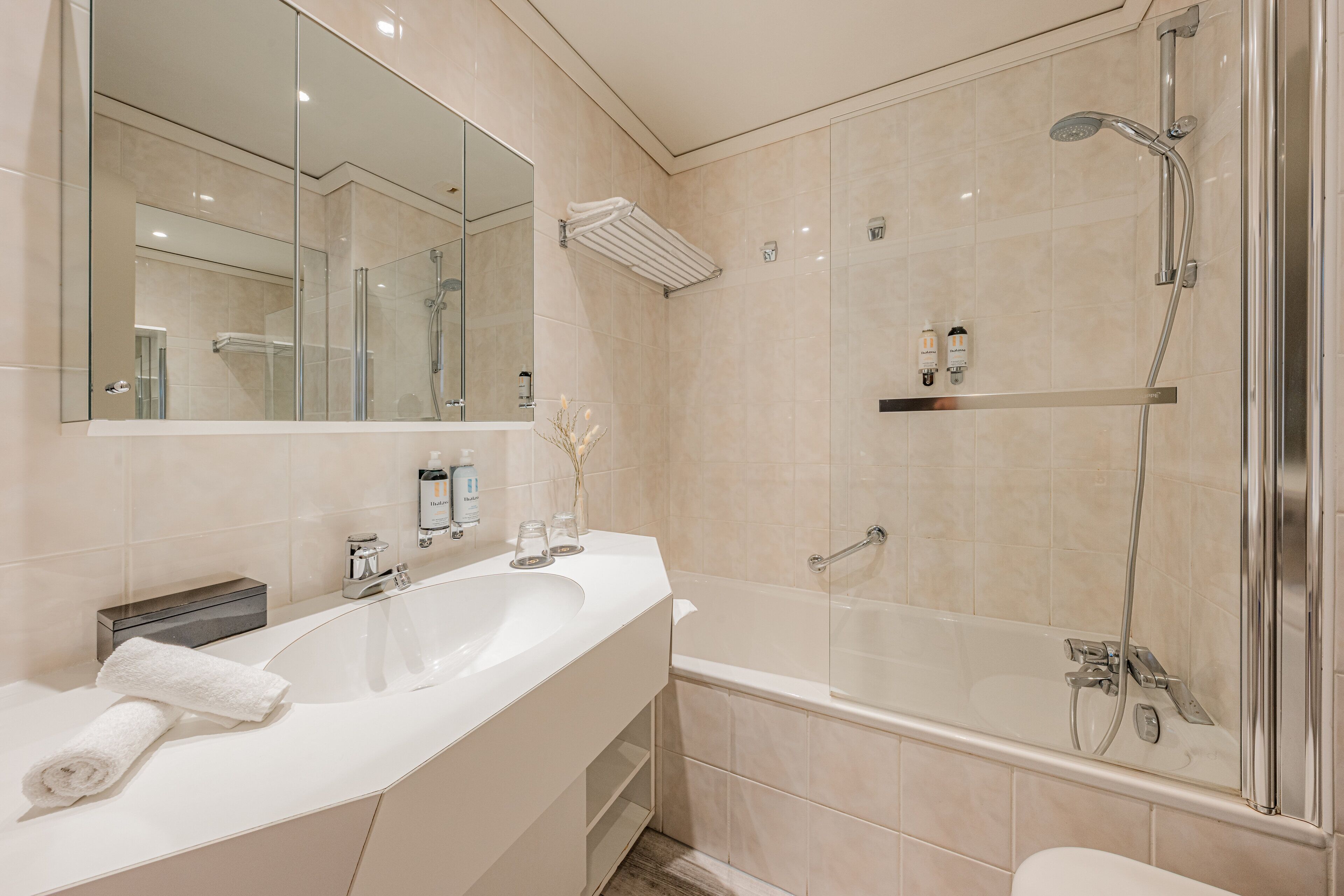 Un baño moderno con un espejo grande, un lavamanos doble, ducha con mampara de vidrio y un perchero para toallas.