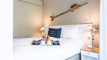Una cama bien hecha con una bandeja de desayuno, una mesita de noche con lámpara y un objeto decorativo en la pared.