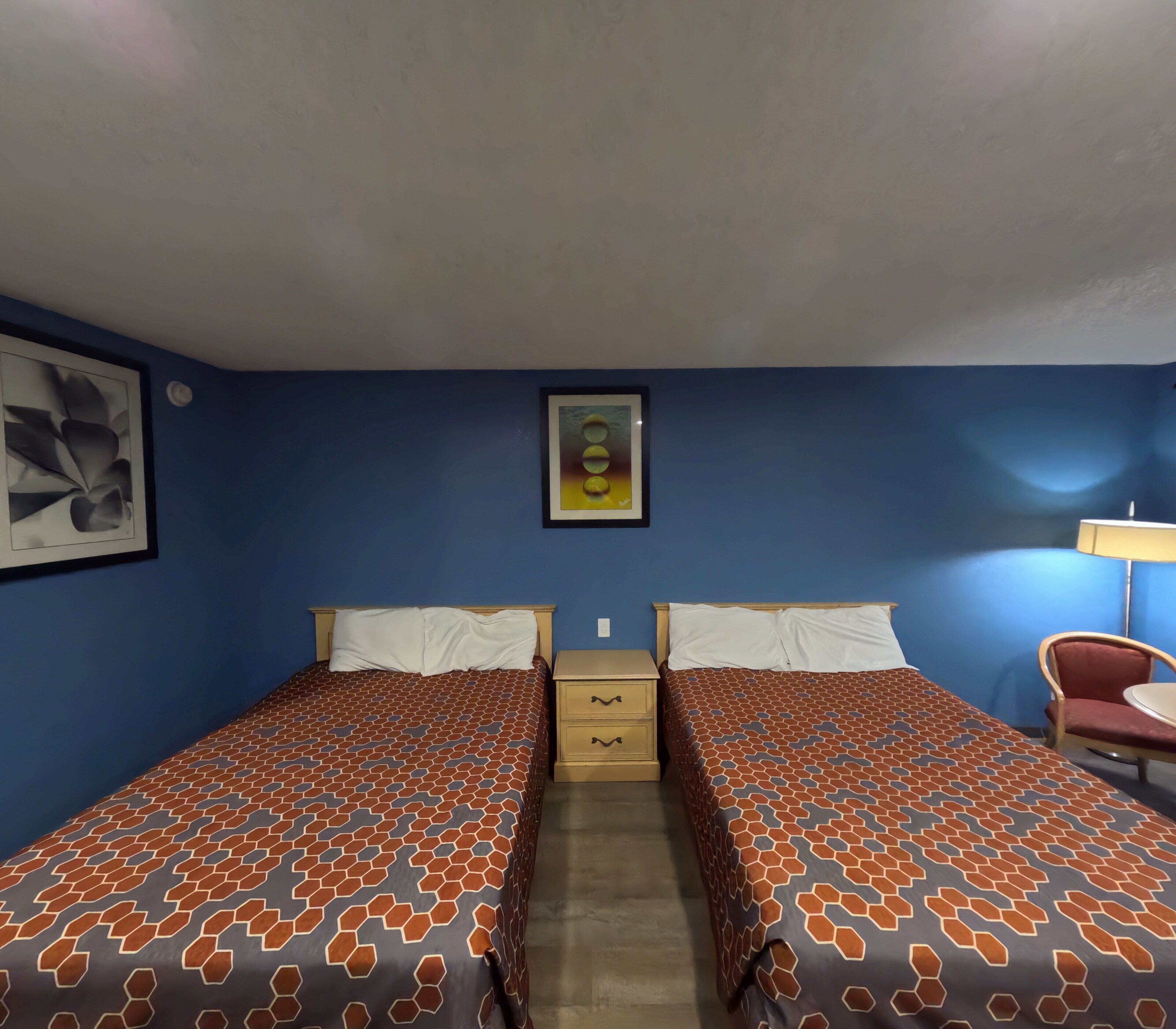 A room with two beds, a chair, a nightstand, and a lamp.