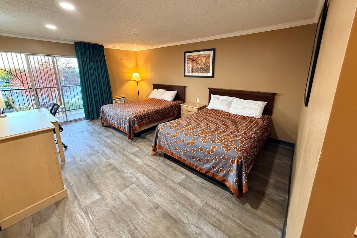 A hotel room with two beds, a desk, a chair, a lamp, and a window with a view.