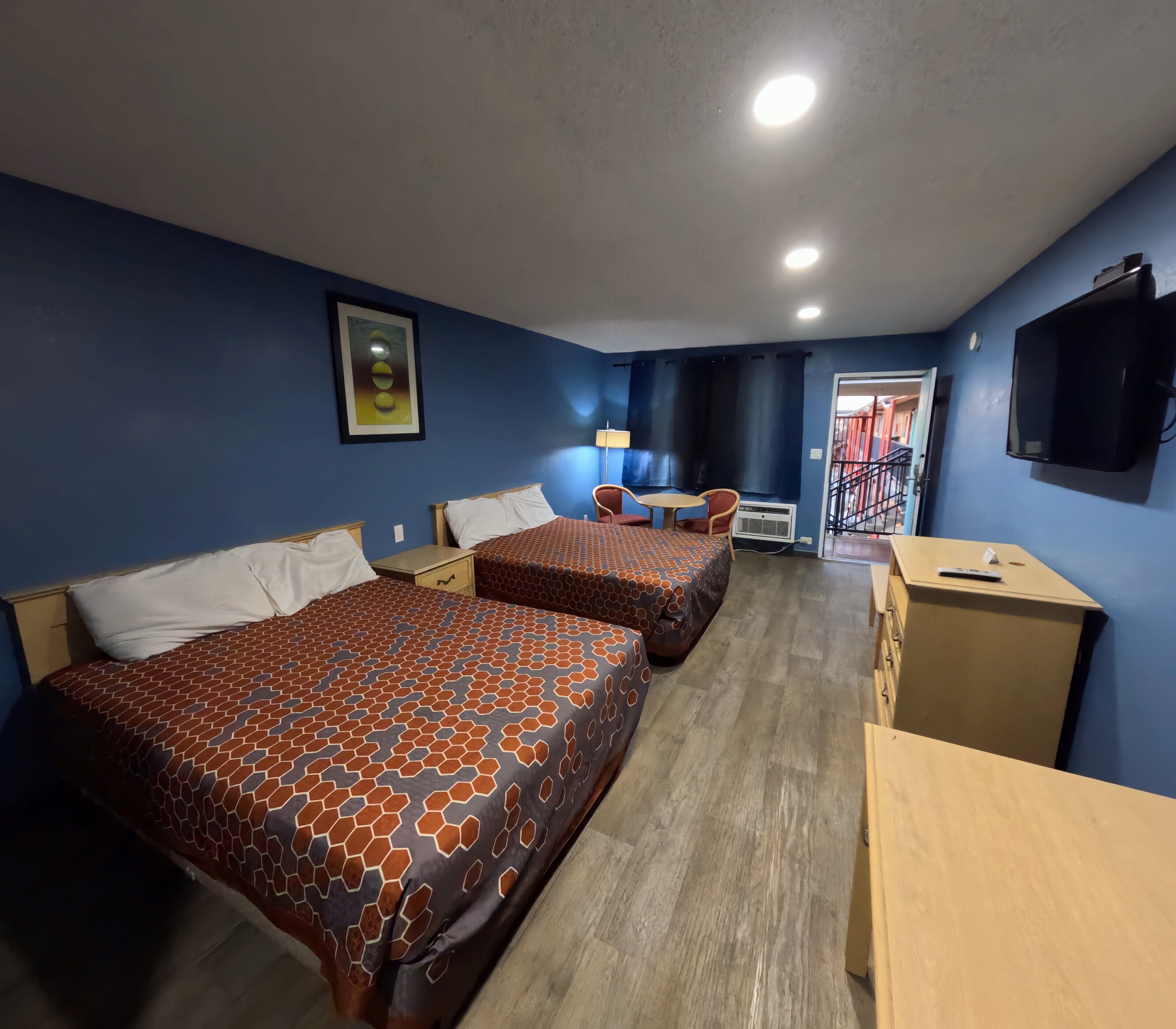 A hotel room with two beds, a desk, a chair, a TV, and a window with curtains.