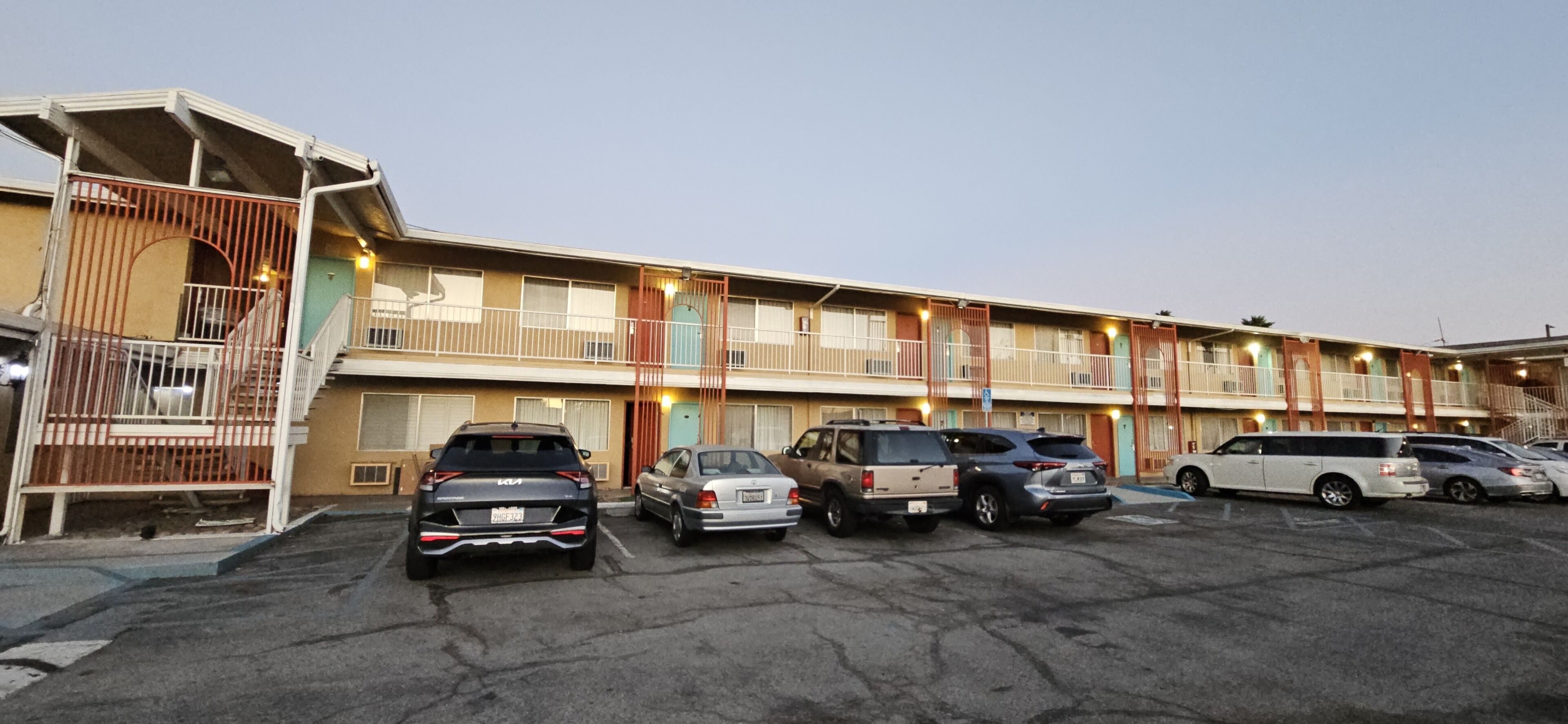 A motel with multiple floors, a parking lot with several cars, and a gated entrance.