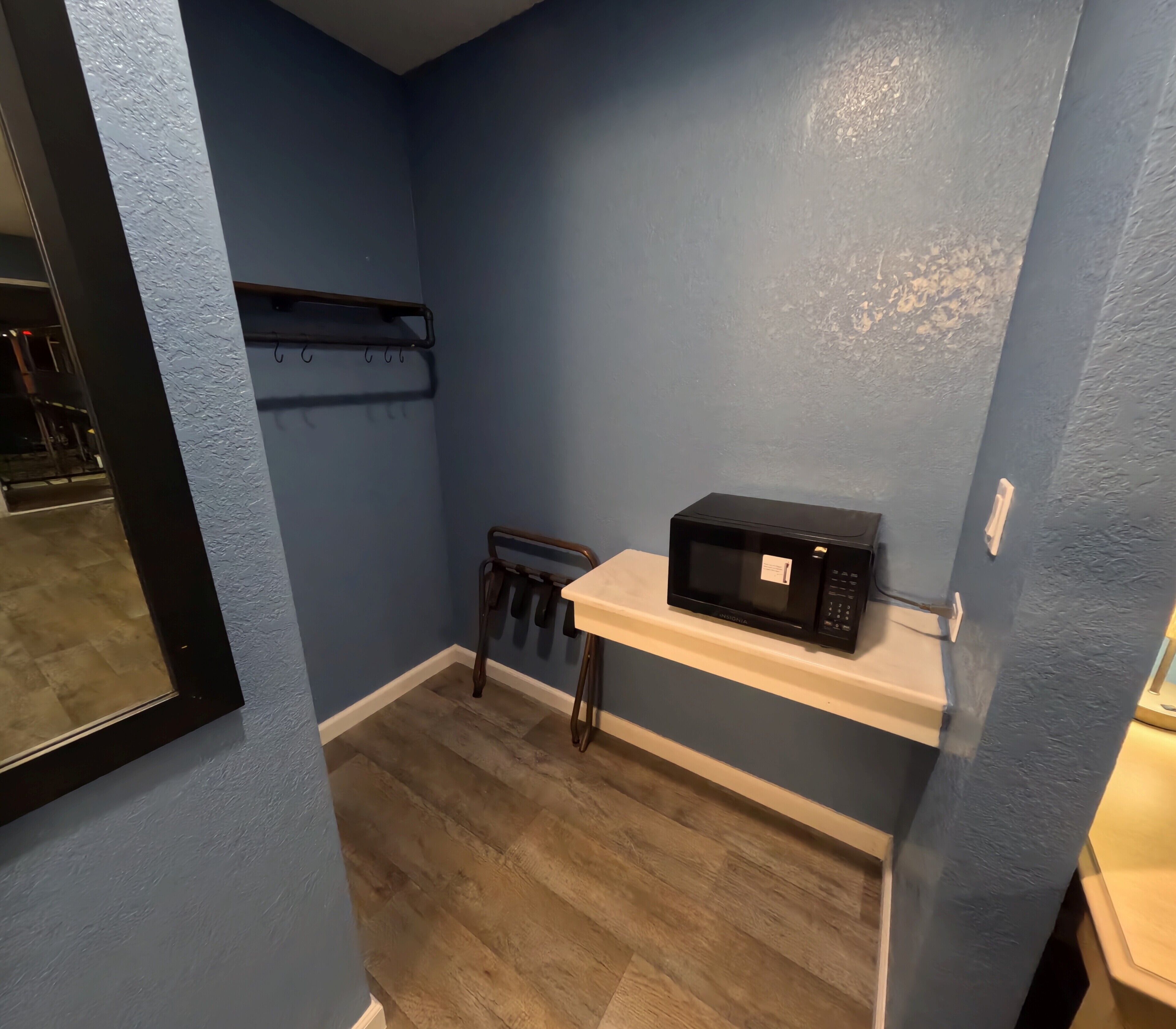 Une petite cuisine équipée d’un micro-ondes posé sur une étagère, d’un porte-ustensiles suspendu et d’une chaise.