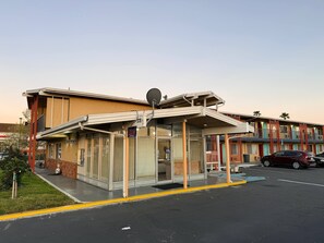 A motel with a glass-enclosed lobby, a satellite dish, and a parking lot.