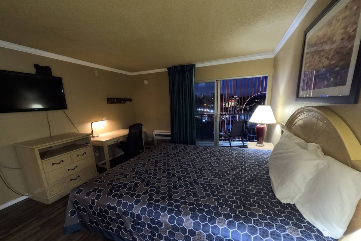 A hotel room with a bed, a desk, a chair, a TV, a window with a view of the city, and a balcony.