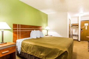 Une chambre d’hôtel avec un lit, deux lampes de chevet, une tête de lit en bois, un mur vert, une porte et une petite table.