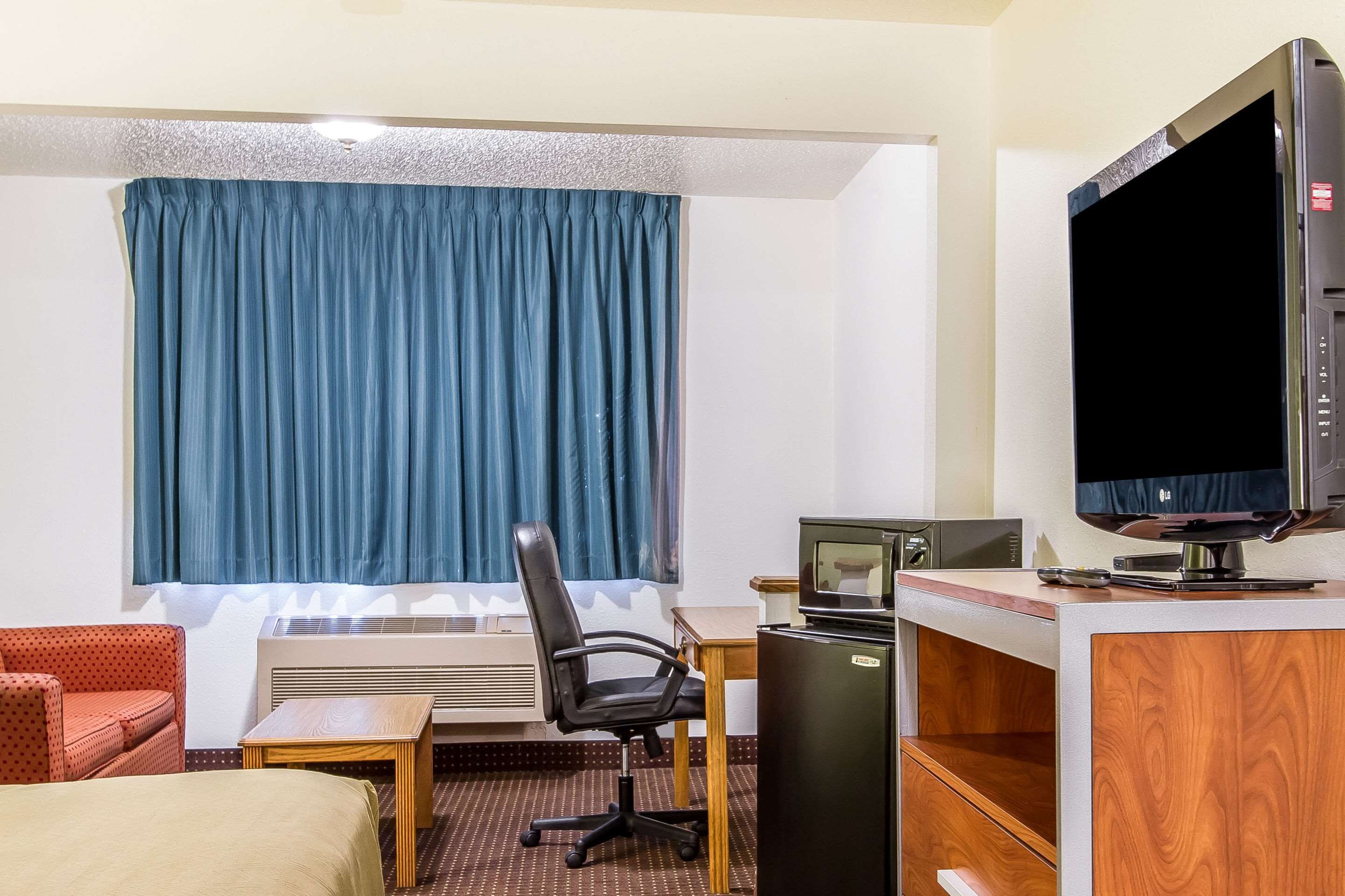 Habitación de hotel con cama, escritorio, silla, televisor y refrigerador pequeño.