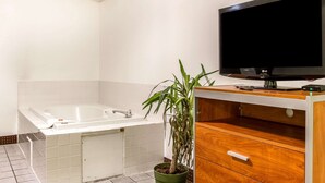 Uma casa de banho moderna com uma banheira, um vaso de plantas verde, uma toucador de madeira com uma televisão de ecrã plano e um chão em mosaico.