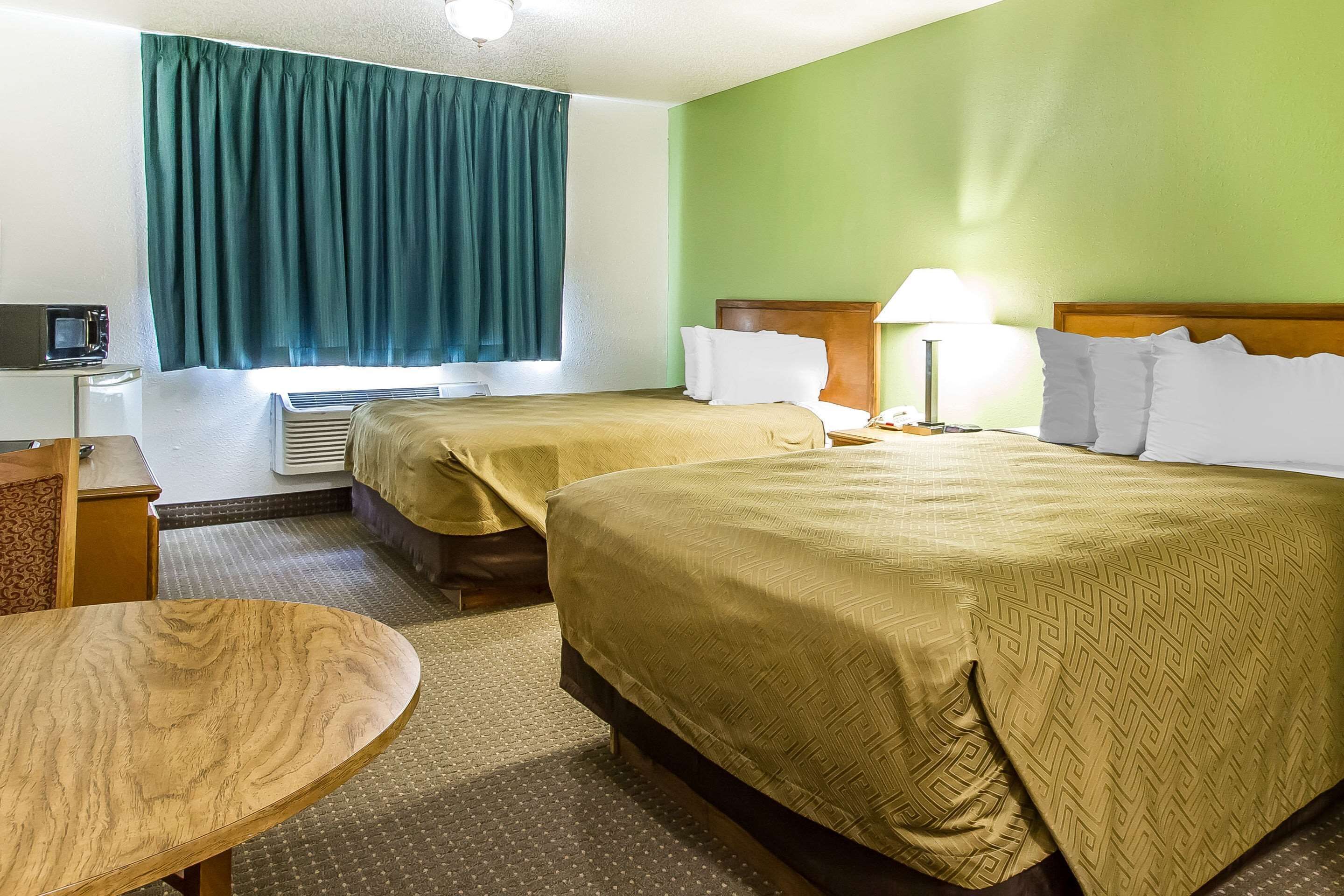 A hotel room with two beds, a desk, a chair, a TV, and a window with curtains.