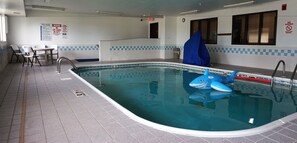 Une piscine avec un flotteur en forme de requin, une chaise de maître-nageur et une table avec des chaises.