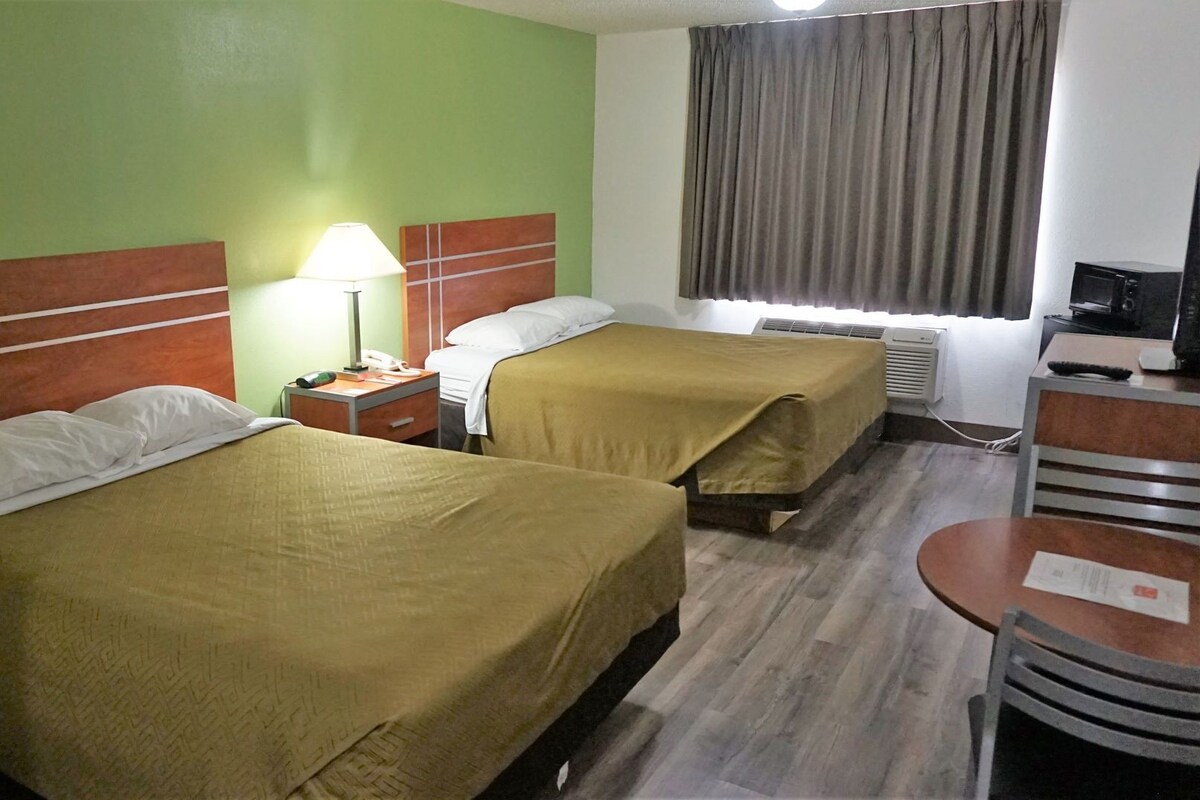 A hotel room with two beds, a desk, a chair, a lamp, a telephone, and a television.