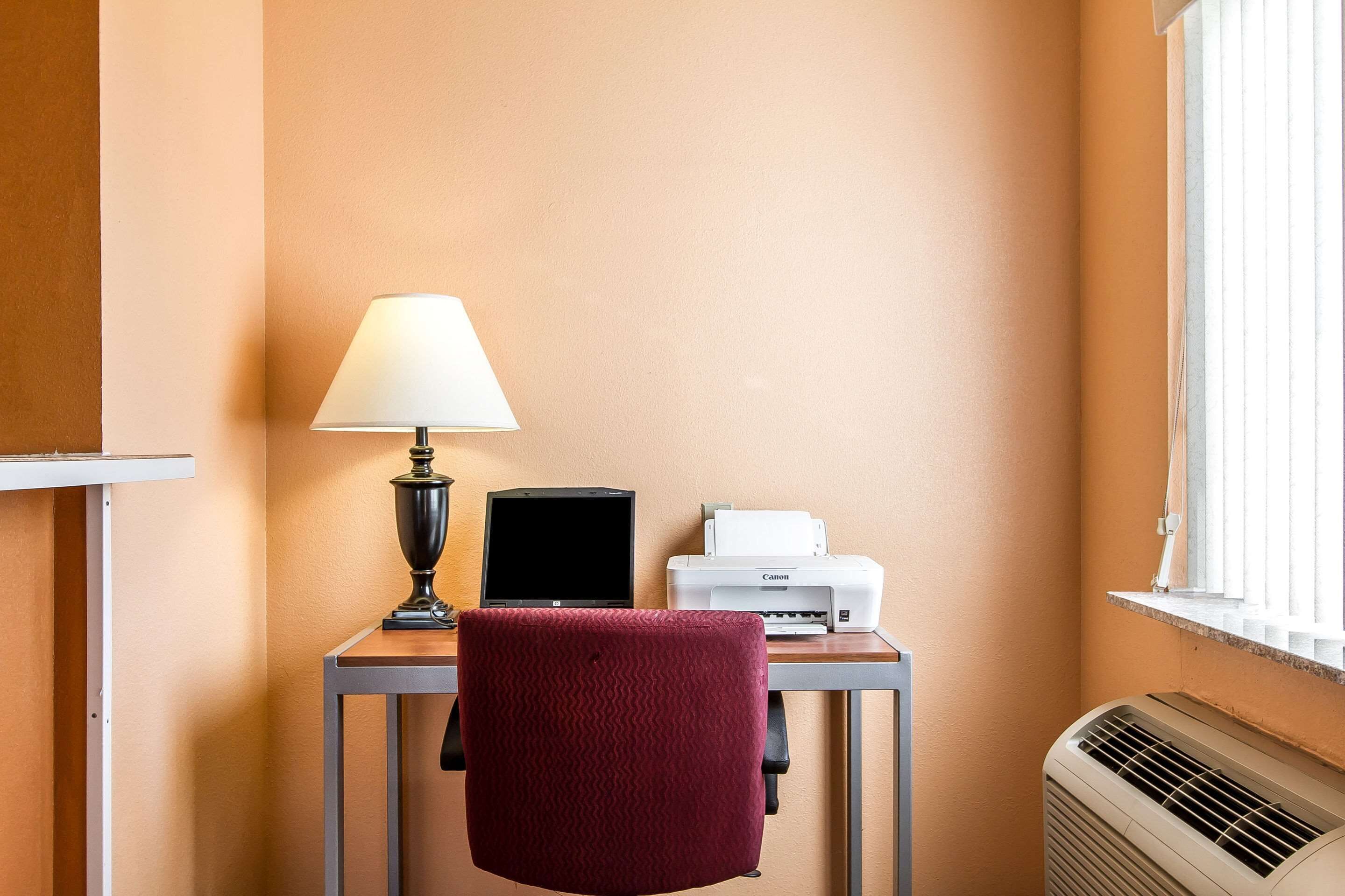 A small workspace with a desk, a chair, a lamp, a laptop, and a printer.