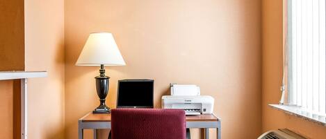 A small workspace with a desk, a chair, a lamp, a laptop, and a printer.
