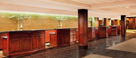Un vestíbulo de hotel con mostrador de recepción, paneles de madera y suelo de baldosas.