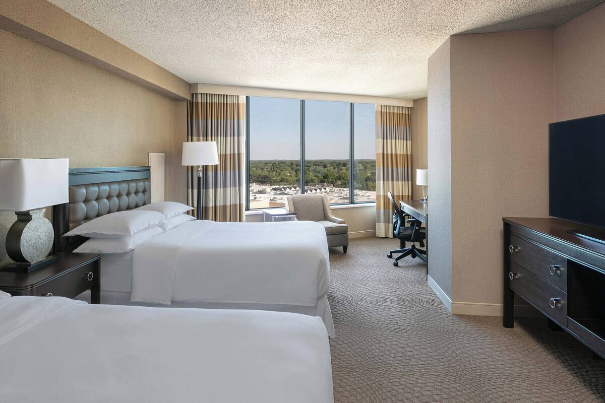 A hotel room with two beds, a desk, a chair, and a TV.
