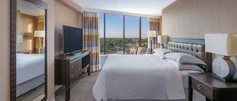 Habitación de hotel con una cama grande, un televisor de pantalla plana, un aparador y vistas a la ciudad.