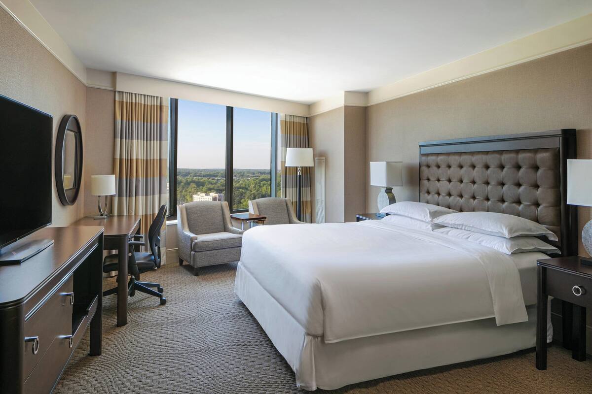 A hotel room with a large bed, a desk, a chair, and a TV.