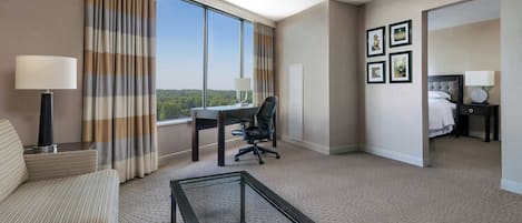 A hotel room with a large window, a desk, a chair, a bed, and a coffee table.