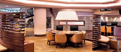 Un moderno vestíbulo de hotel con un mostrador de recepción curvo, una mesa redonda con sillas y una lámpara de pie grande.