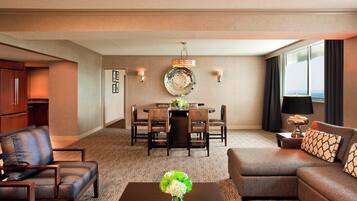A hotel room with a dining area, a sofa, a coffee table with a vase, and a view of the city.