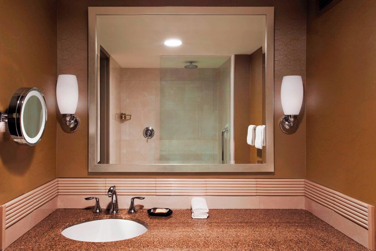 A bathroom with a large mirror, two wall-mounted lights, a sink, and a shower area.