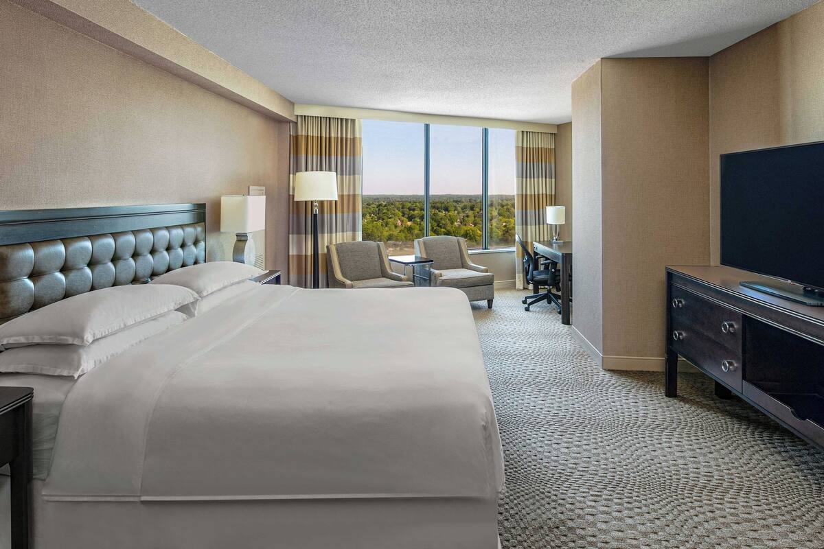 A hotel room with a large bed, two armchairs, a desk, and a TV.