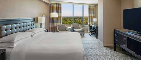 Une chambre d’hôtel avec un grand lit, deux fauteuils, un bureau et une télévision.