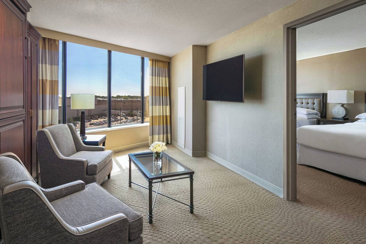 A hotel room with a large window, a flat-screen TV, a bed, a sofa, and a coffee table.