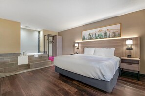 Habitación de hotel con una cama grande, baño con bañera y un cuadro en la pared.