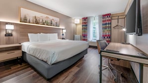 A hotel room with a bed, bedside tables, a desk, a chair, a TV, and a painting on the wall. - Quality Inn Morgantown (Morgantown)