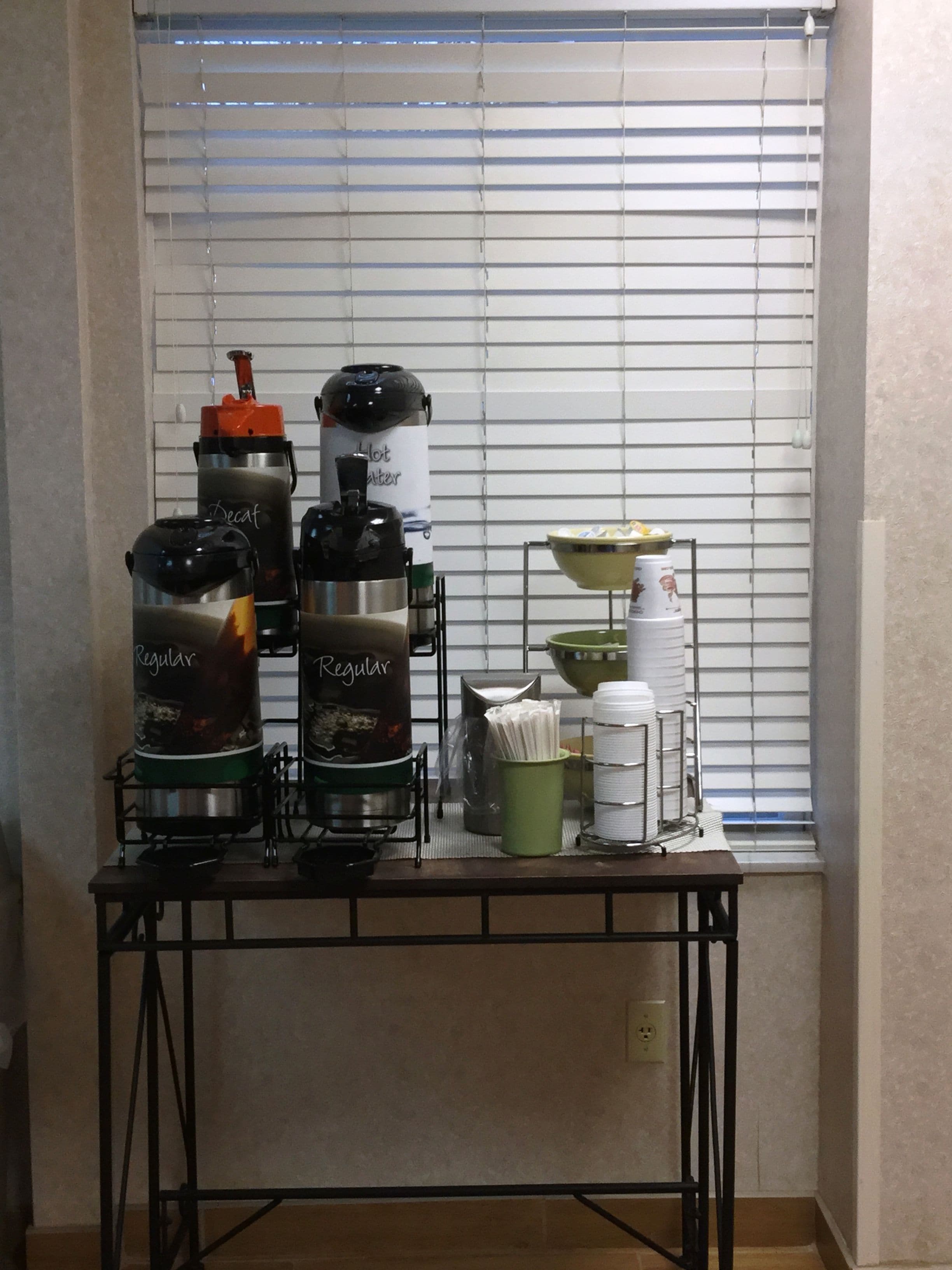 A kitchenette with coffee makers, a kettle, and a coffee dispenser on a table.