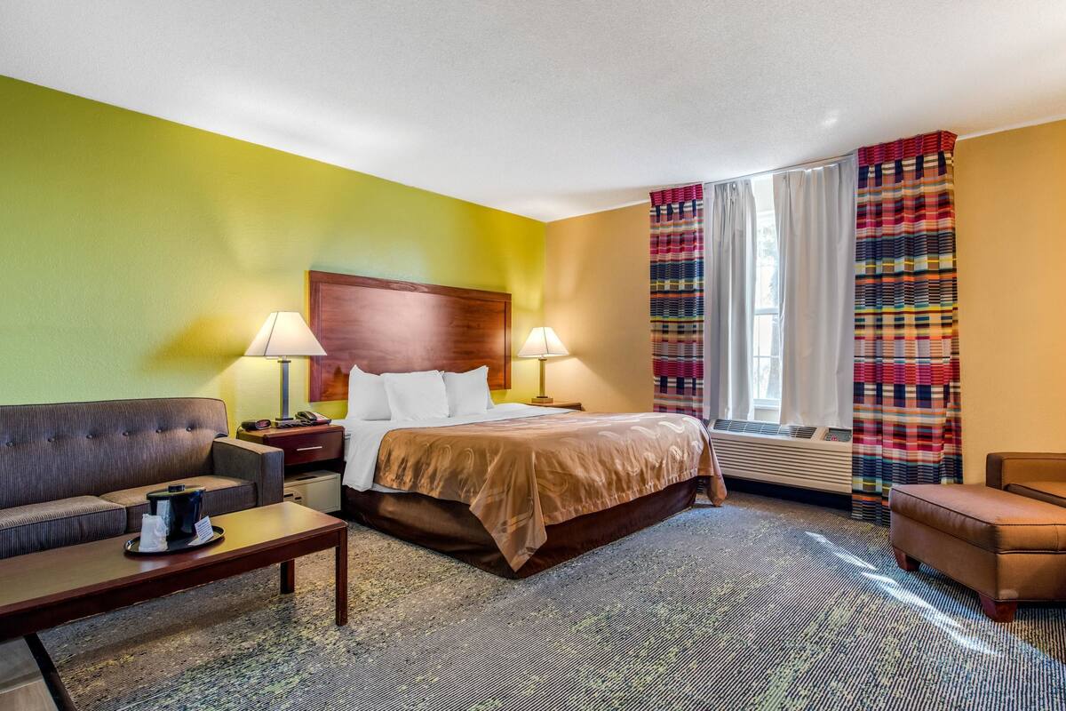 A hotel room with a bed, two bedside tables, a sofa, a chair, and a window with curtains.
