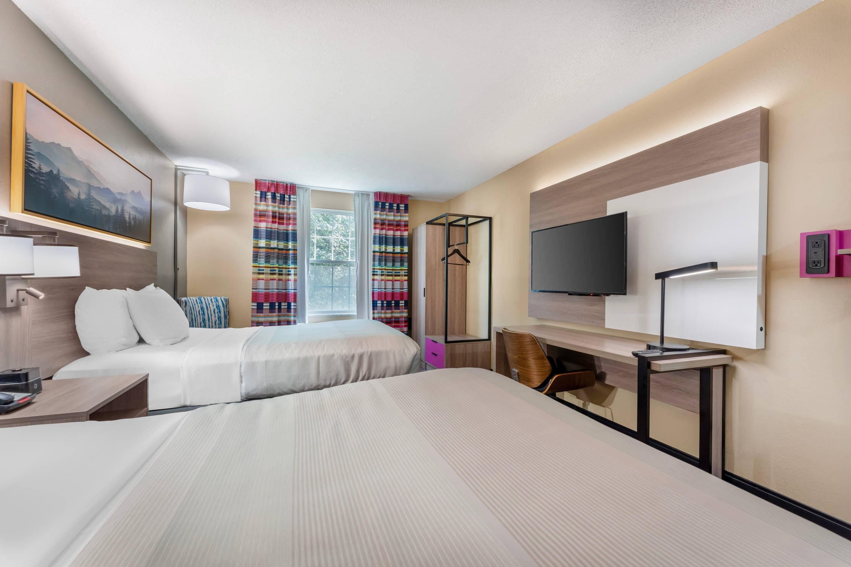 Een hotelkamer met twee bedden, een bureau, een stoel, een televisie en een raam met gordijnen.