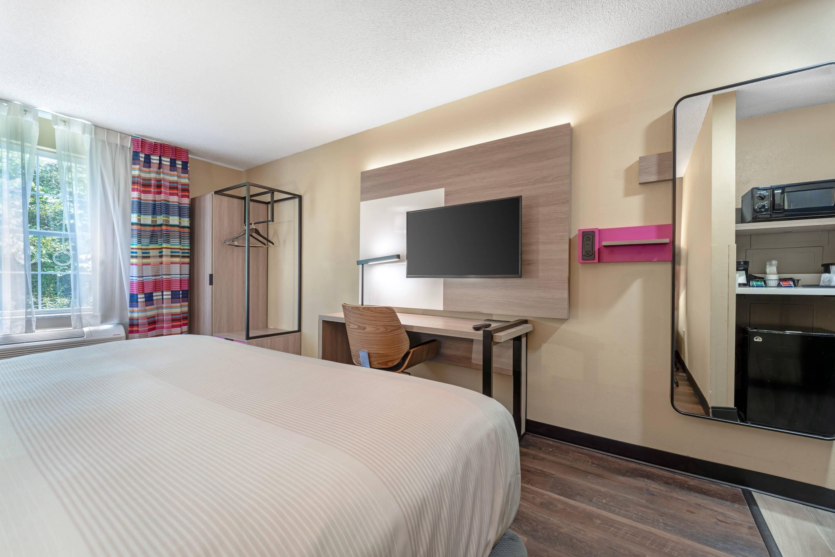 A hotel room with a large bed, a desk with a chair, a flat-screen TV, a microwave, and a mini-fridge.