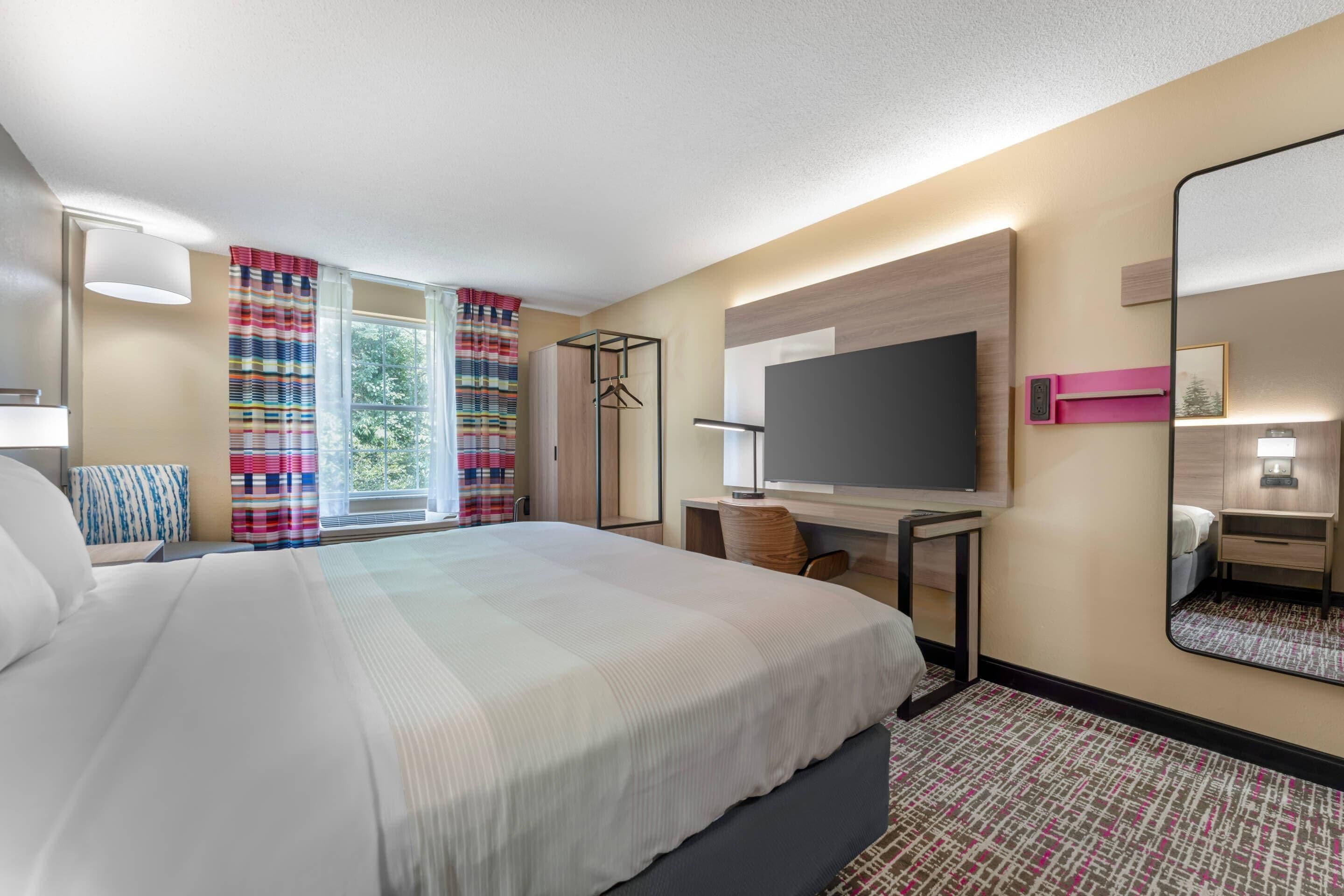 Habitación de hotel con cama, escritorio, televisor y espejo.