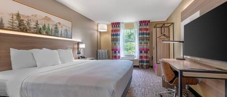 A hotel room with a large bed, a desk with a flat-screen TV, a coat rack, and a window with curtains.