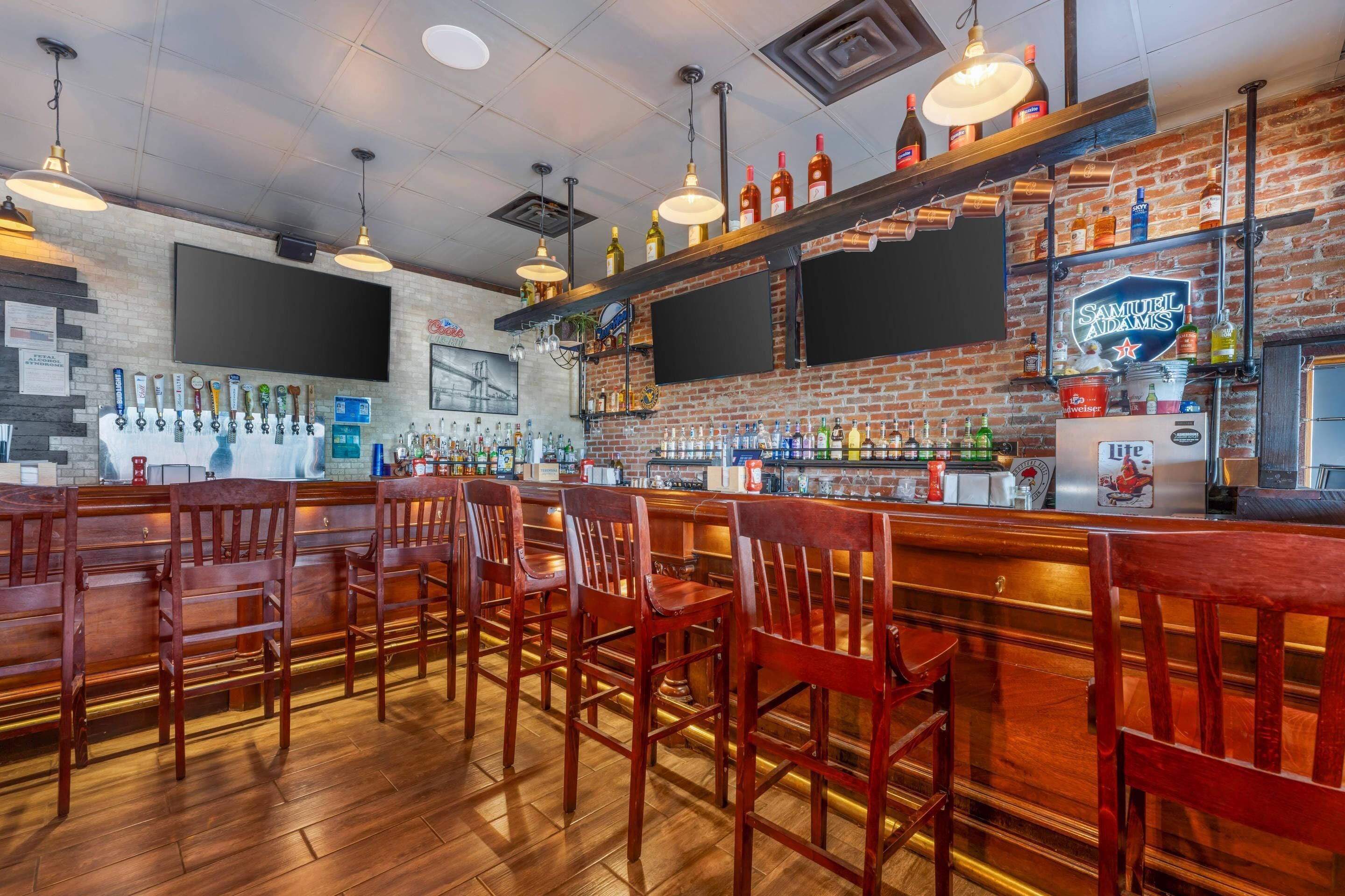 A bar with wooden chairs, a brick wall, and various bottles on shelves.