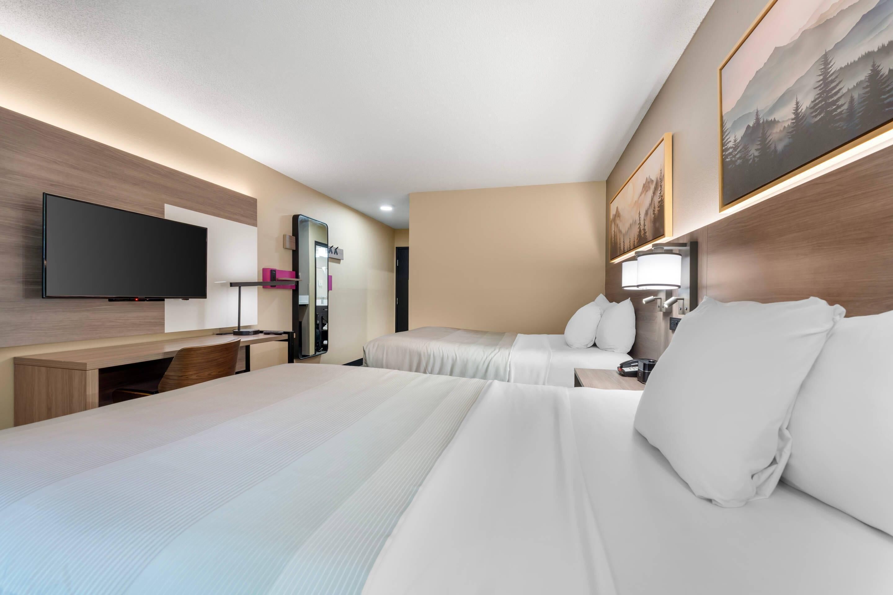 A hotel room with two beds, a flat-screen TV, a desk with a computer, and a mirror.