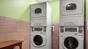 Una sala de lavandería con dos lavadoras apiladas, un banco de madera y una pared de azulejos.