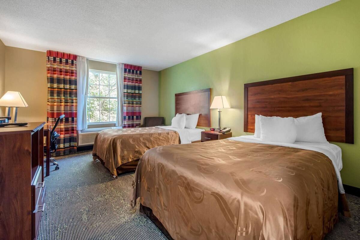 A hotel room with two beds, a desk, and a chair.
