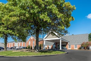 A brick building with a covered parking area and a large tree in front.