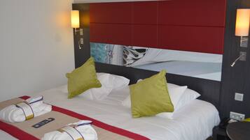 Habitación de hotel con una cama grande, dos almohadas, cabecera roja y una lámpara fijada a la pared.