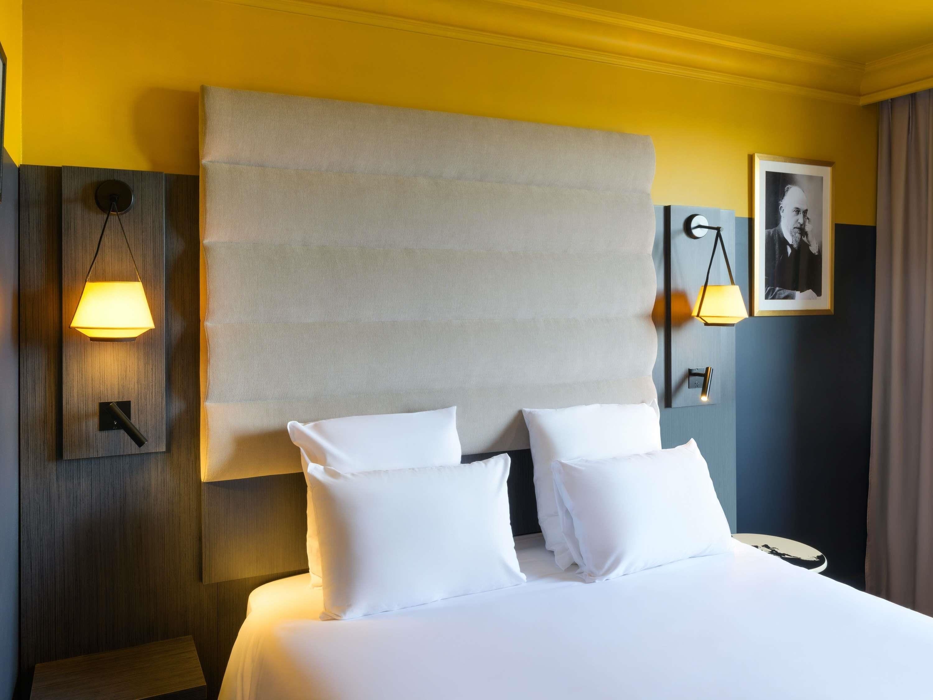 A hotel room with a large bed, two bedside tables, a wall-mounted lamp, and a framed picture.