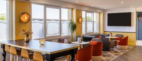 A modern hotel room with a dining area, a sofa, and a large TV screen.